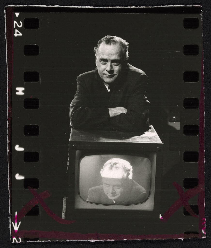 Marshall McLuhan leaning on a TV. The TV is showing an image of Marshall McLuhan.